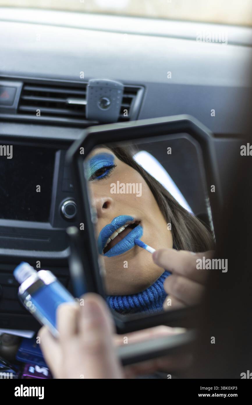 Nahaufnahme einer jungen Frau, die sich in einem Auto schminkt, mit Blautönen, die in einen Spiegel schauen Stockfoto