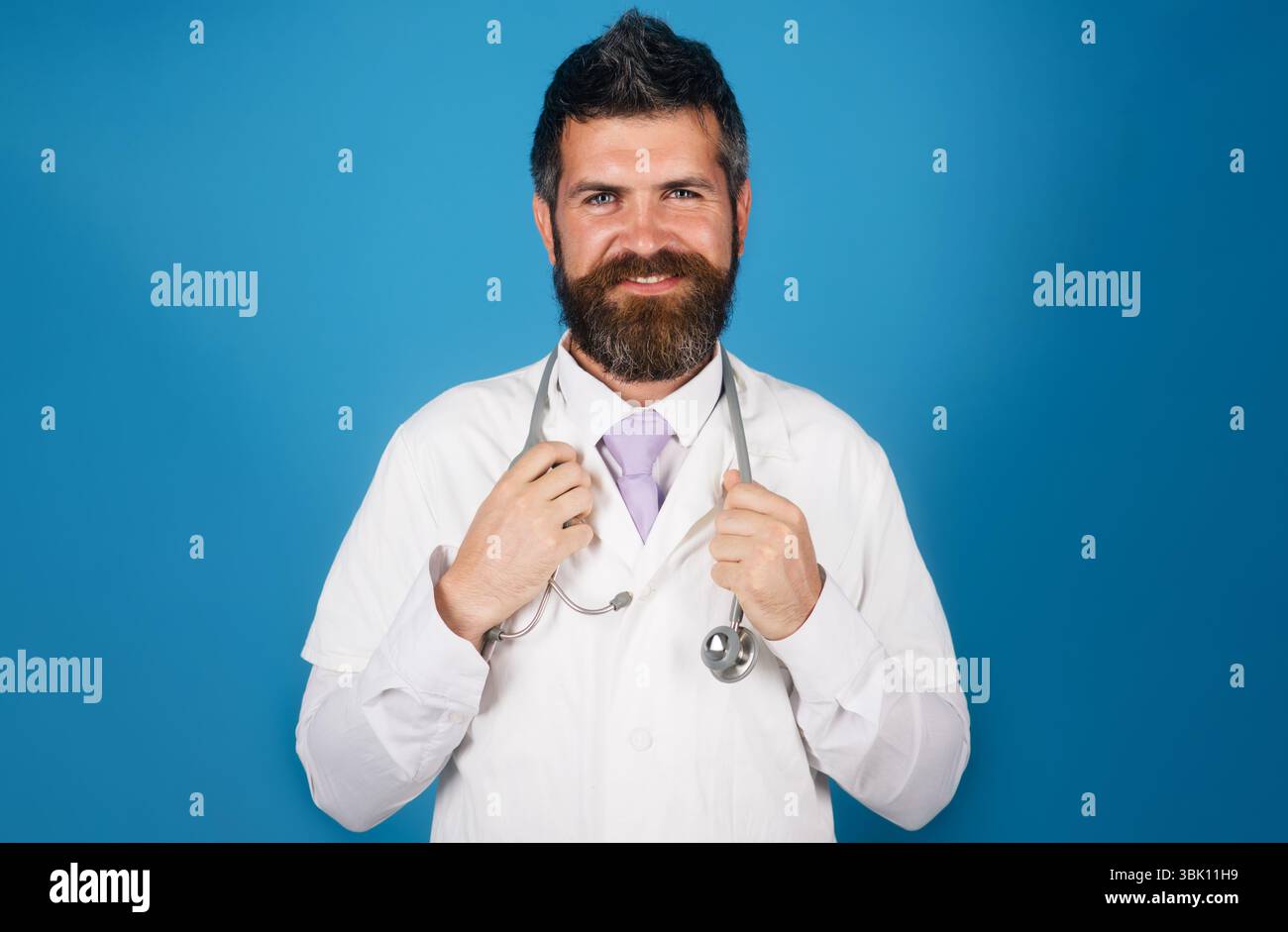 Lächelnder Arzt mit Bart und Schnurrbart im medizinischen Kleid mit Stethoskop im Krankenhaus. Gesundheitswesen, Klinik, Medizin, Behandlung und medizinisches Personal Stockfoto