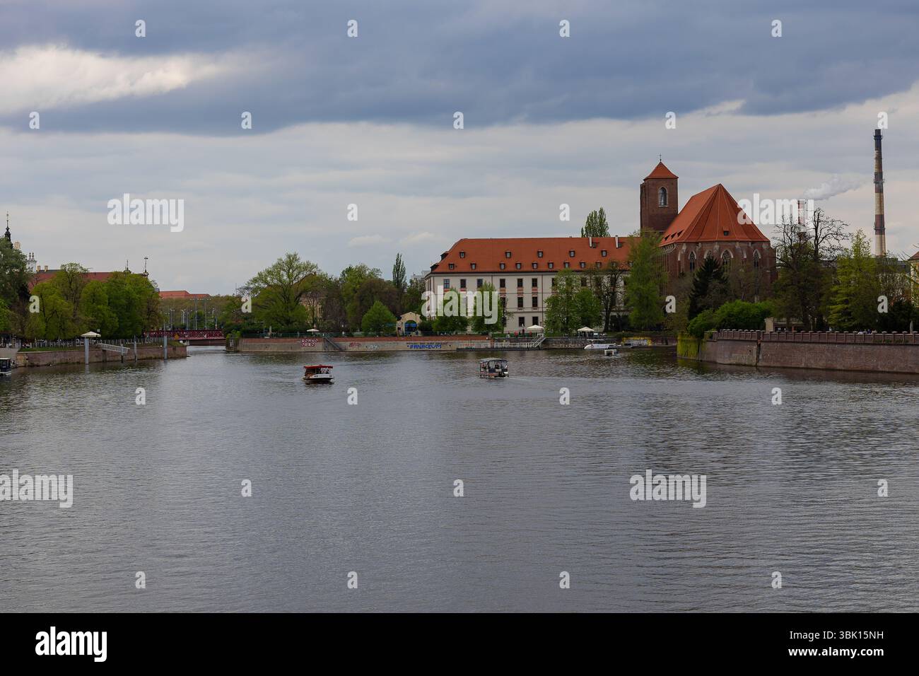 Malerischer Blick auf den Fluss mit historischen Gebäuden mit roten Dächern und Kirche an bewölkten Tagen in der europäischen Stadt. Architektonisches Erbe und urbane Uferpromenade Stockfoto