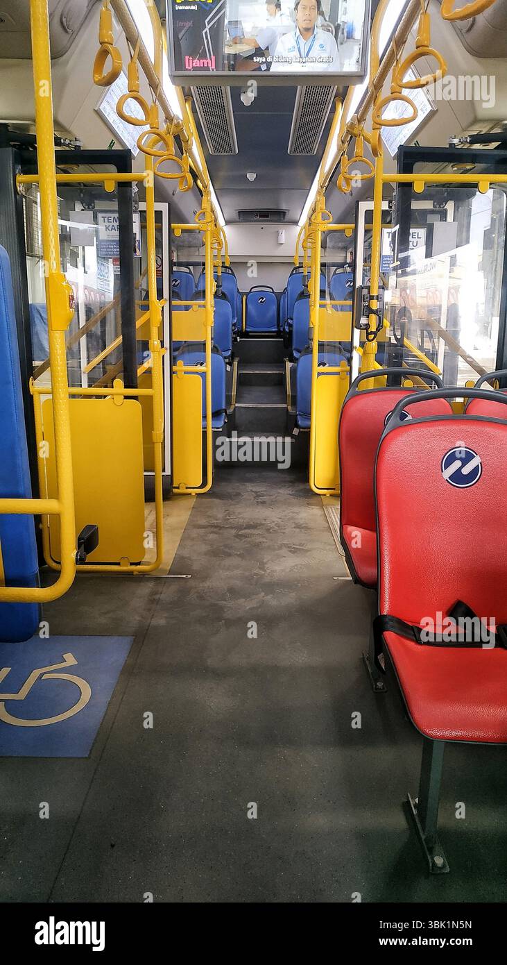 Innenansicht eines modernen elektrischen Stadtbusses mit sauberen, organisierten Sitzgelegenheiten und barrierefreien Merkmalen. Hellgelbe Stangen und kontrastierender Sitz Stockfoto