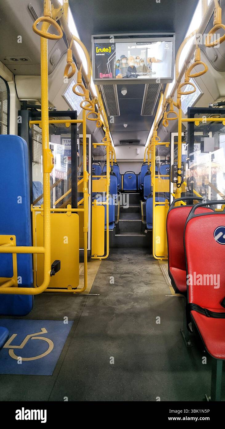 Innenansicht eines modernen elektrischen Stadtbusses mit sauberen, organisierten Sitzgelegenheiten und barrierefreien Merkmalen. Hellgelbe Stangen und kontrastierender Sitz Stockfoto