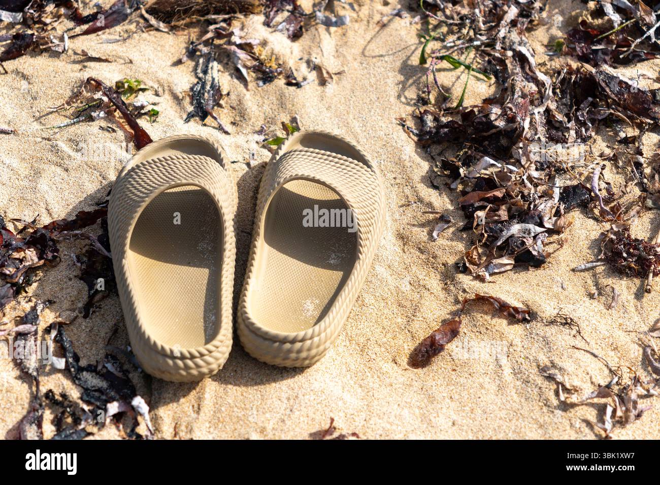 Zwei braune Sandalen liegen auf dem Sand. Die Sandalen werden nicht benutzt und bleiben zurück Stockfoto