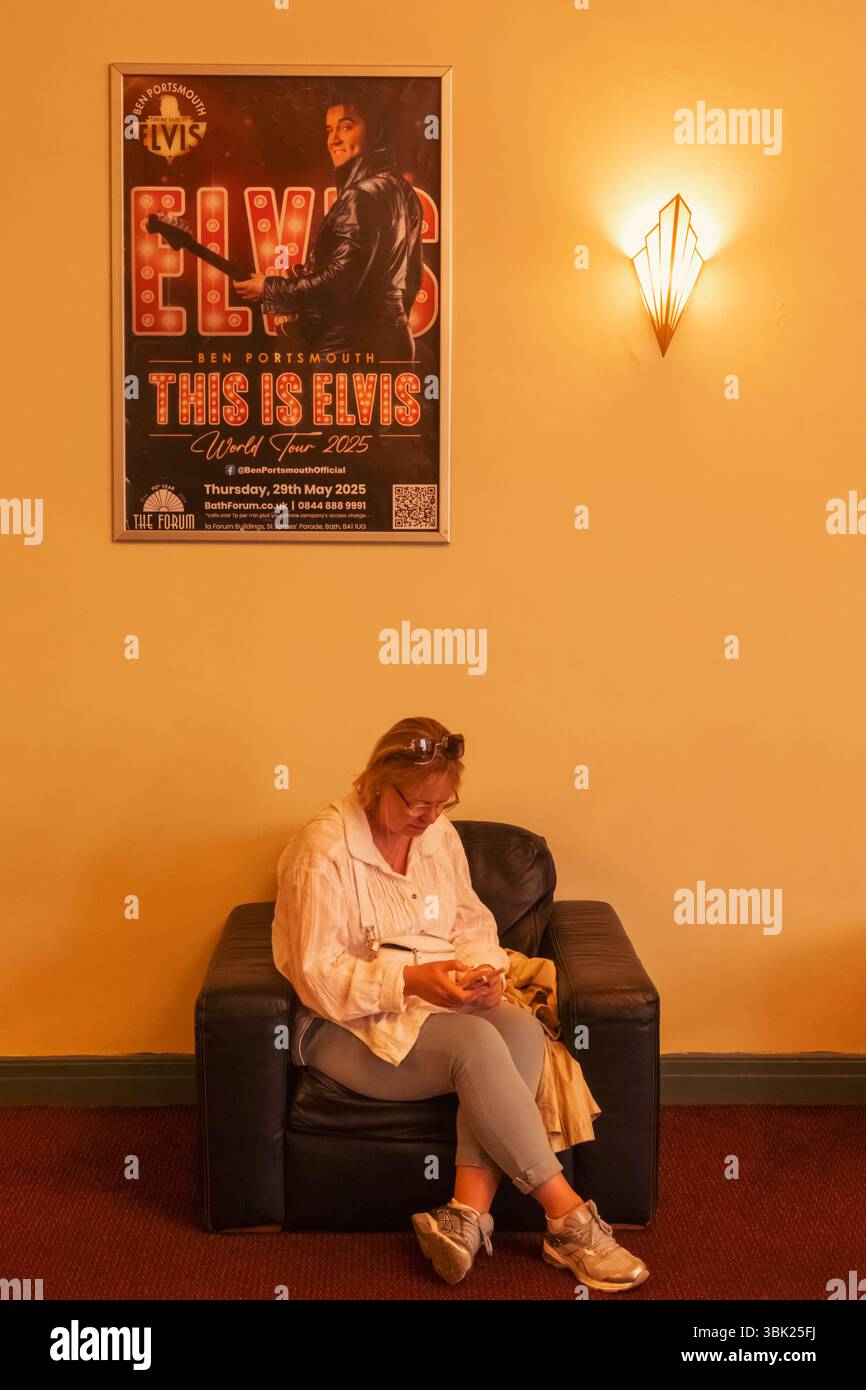 England, Somerset, Bath, The Forum, Innenansicht einer Frau, die unter Elvis-Showplakat sitzt und Art déco-Lampe Stockfoto England, Somerset, Bath, The Forum, Innenansicht einer Frau, die unter Elvis-Showplakat sitzt und Art déco-Lampe Stockfoto