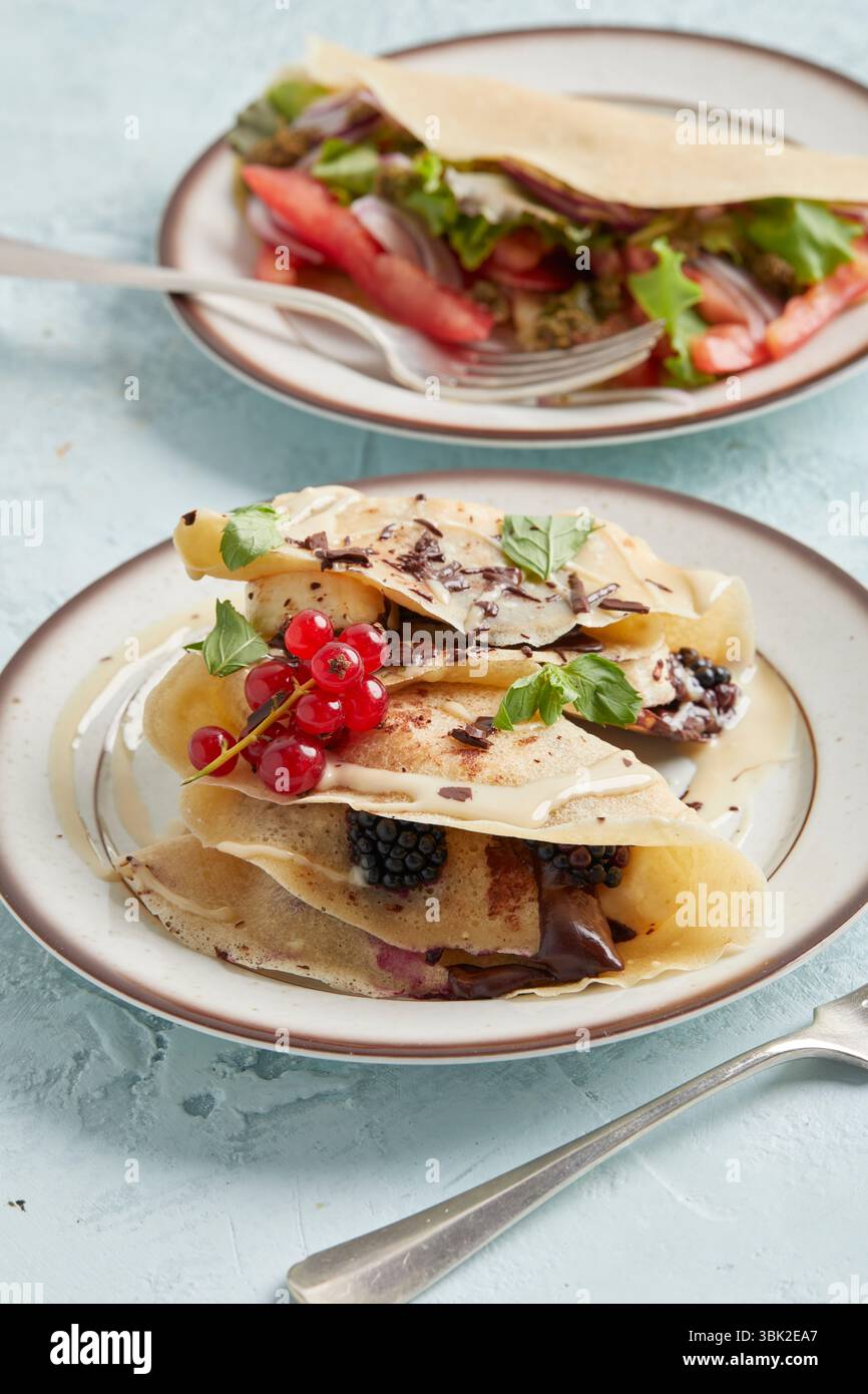 Ein Teller mit süßen und herzhaften Pfannkuchen – eine kreative Brunch-Idee mit Schokolade, Obst, Salat und Tomaten Stockfoto