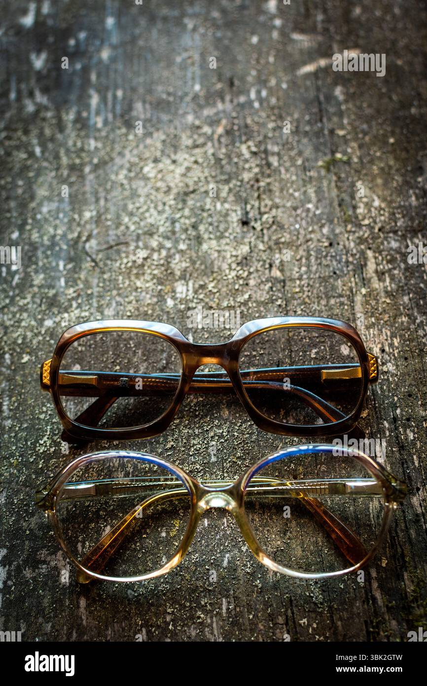 Eine Kollektion von Vintage-Brillen liegt auf einer rustikalen Holzoberfläche, die von warmen Lichtern beleuchtet wird, die ihr einzigartiges Design und ihren Charme hervorheben Stockfoto