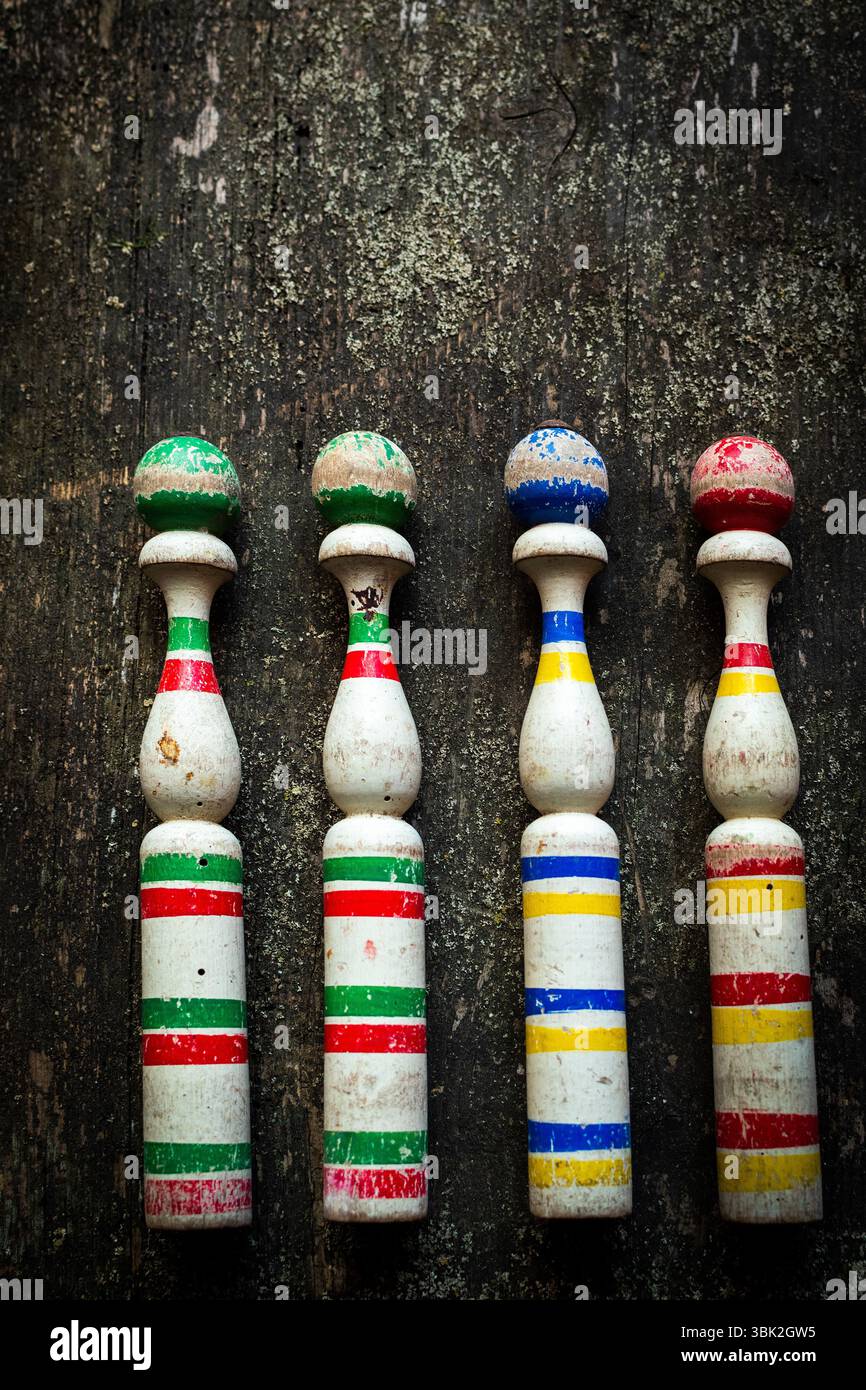 Vier Vintage-Bowlingnadeln aus Holz mit lebhaften Farben sitzen in einer Reihe auf einer rustikalen Holzoberfläche Stockfoto