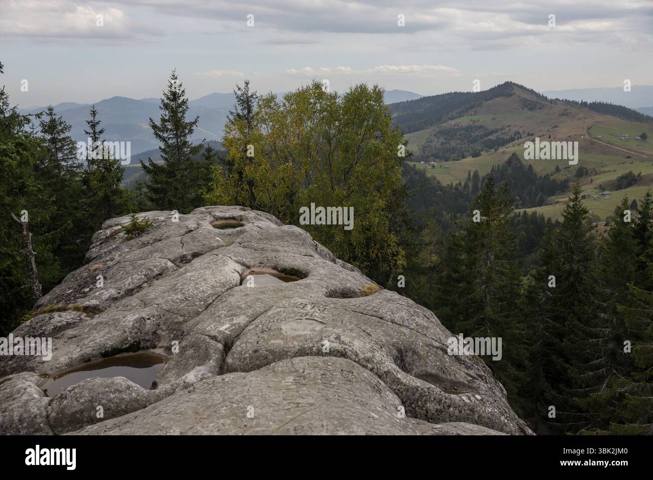 Eine große Felsformation bietet einen Panoramablick auf ferne Berge und üppige Wälder und fängt die ruhige Schönheit der Natur an einem bewölkten Tag ein. Stockfoto