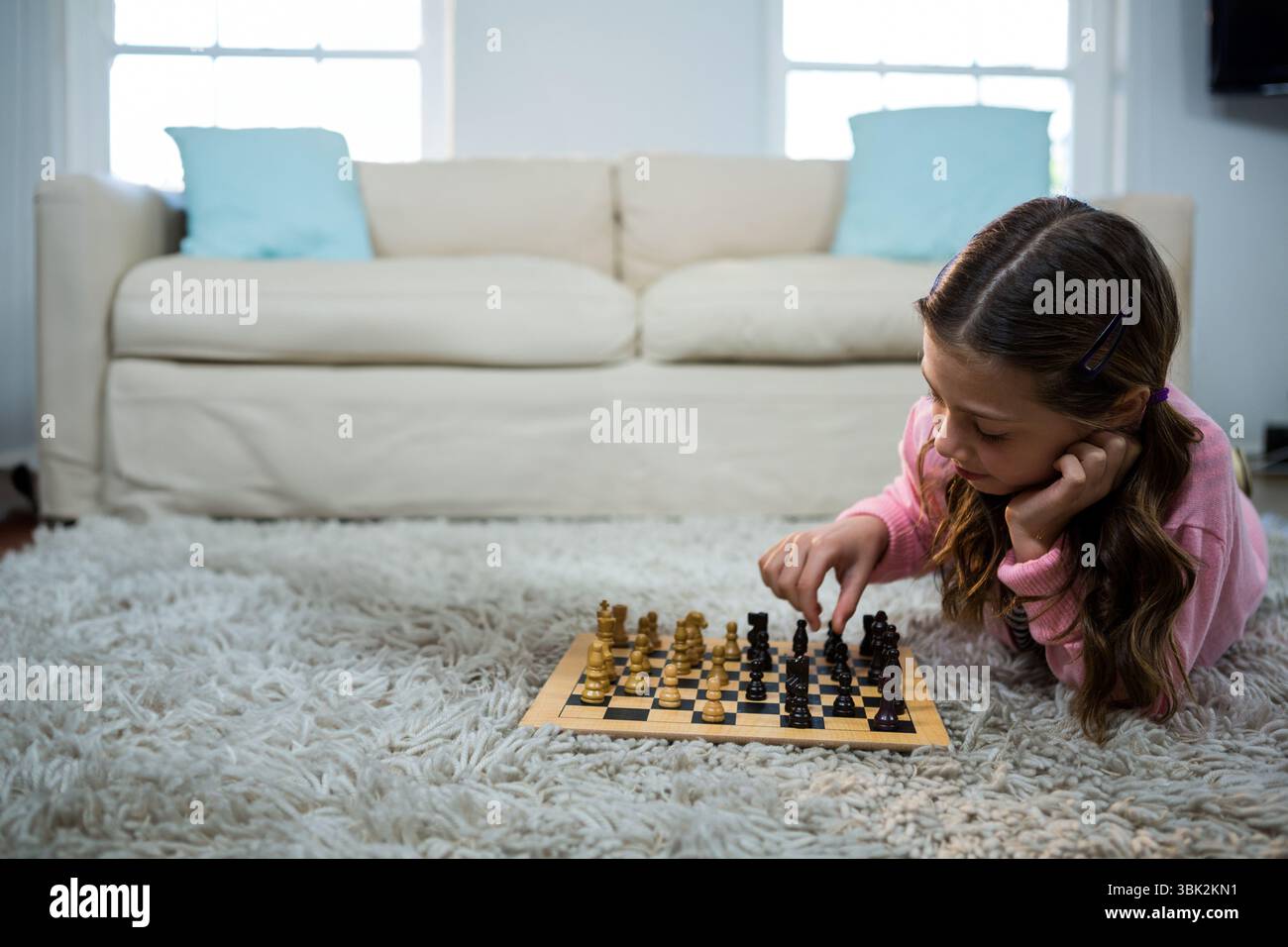Kinder spielen Schach auf weißem Teppich im Wohnzimmer, umgeben von beigefarbenem Sofa und Kissen Stockfoto