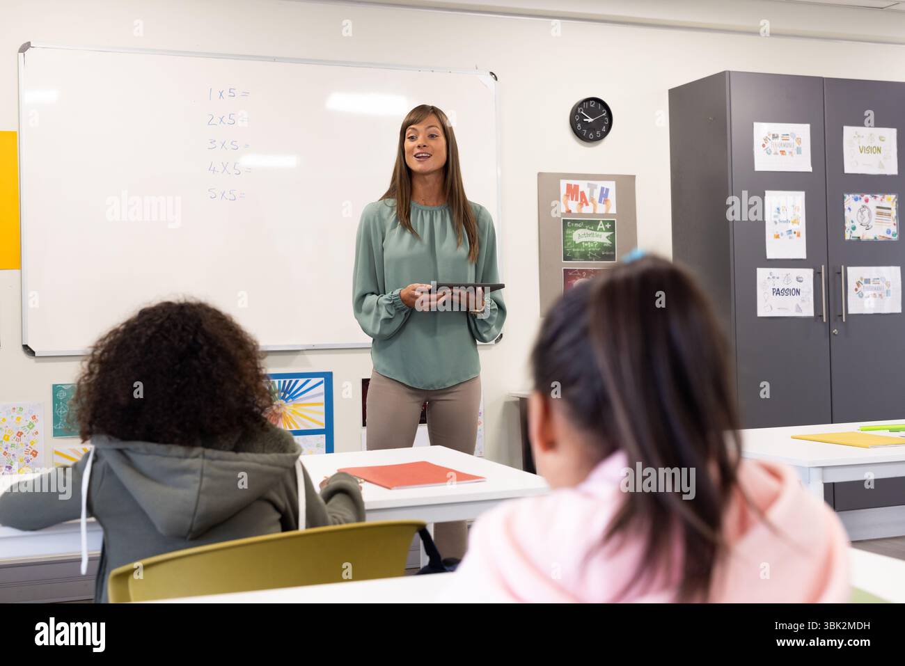 Lehrerin engagiert verschiedene Schüler im Unterricht, hält ein Tablet, diskutiert Mathematik, in der Schule Stockfoto