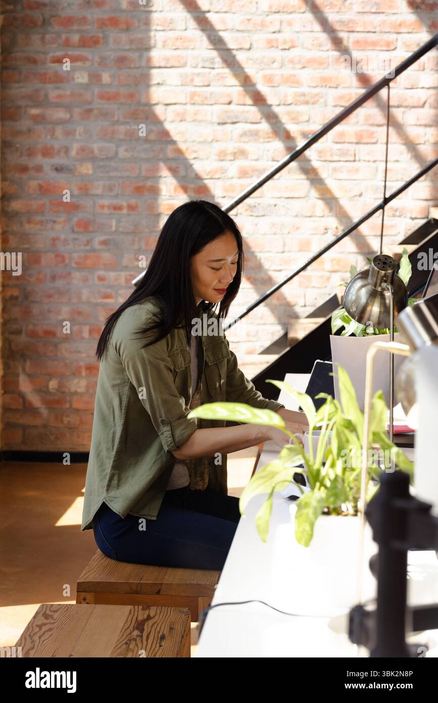 Asiatische Frau codiert auf einem Laptop am modernen Schreibtisch, konzentriert und produktiv Stockfoto