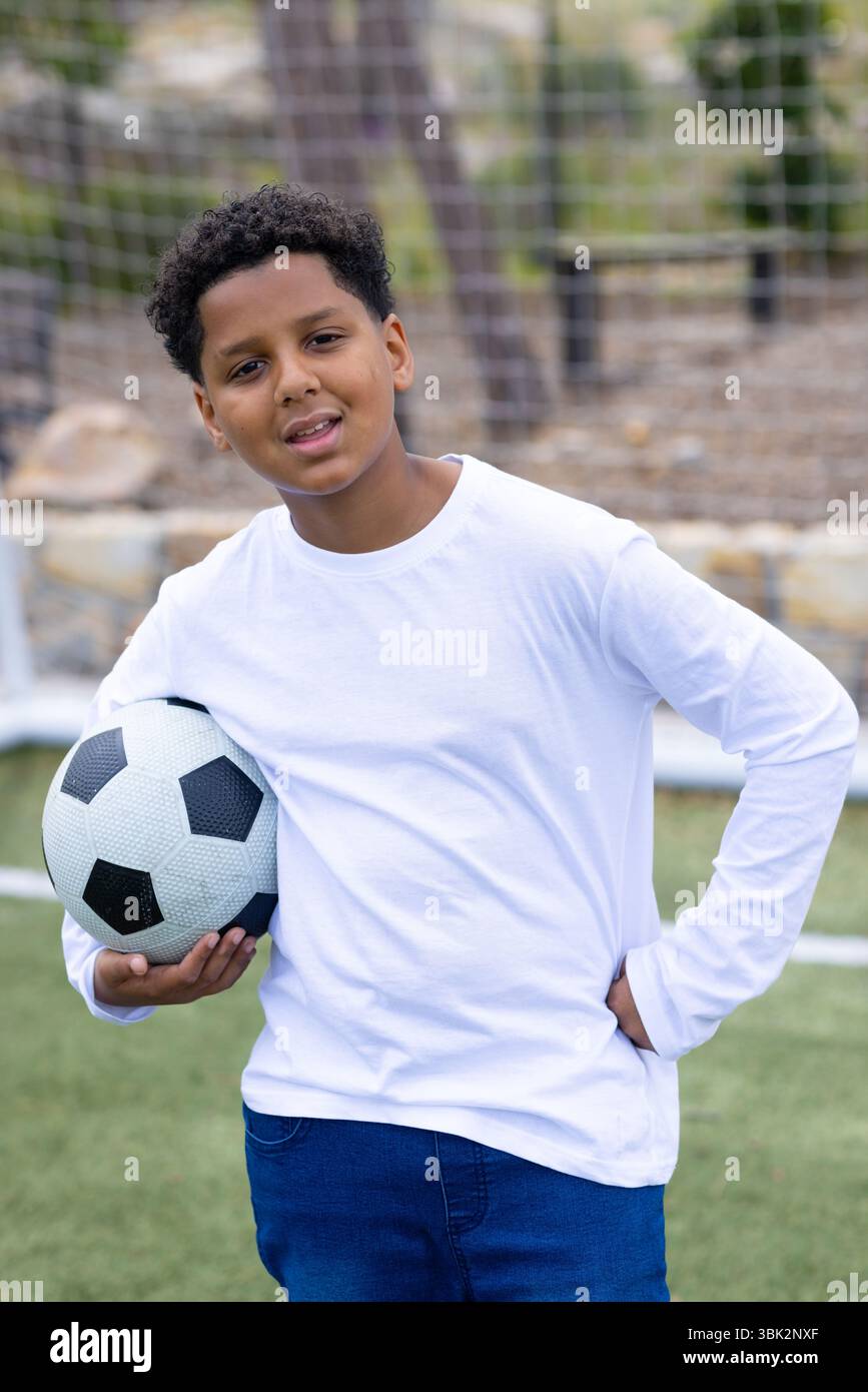Junge, der Fußball auf dem Spielfeld hält und selbstbewusst lächelt während der Schulsportaktivität Stockfoto