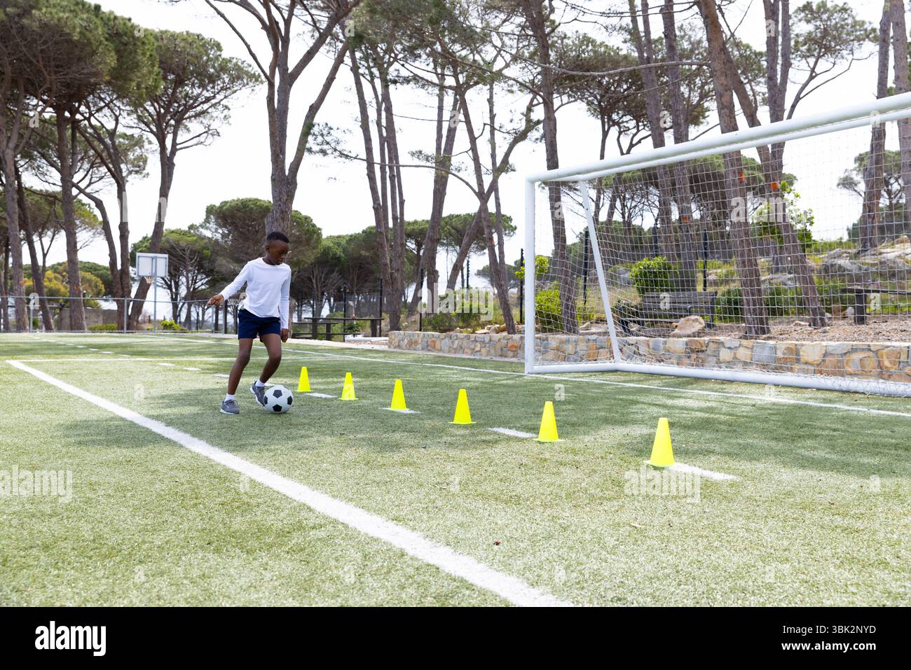 Fußball üben, afroamerikanischer Junge, der auf dem Feld durch Kegel dribbelt, konzentriert und entschlossen Stockfoto
