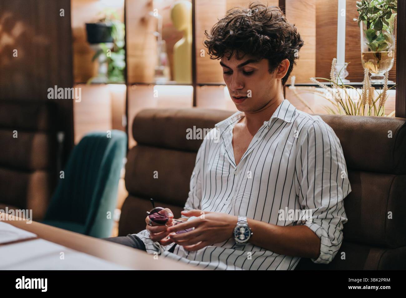 Der junge Mann sitzt allein in einem Restaurant und wartet geduldig auf sein Date. Die Atmosphäre ist modern und einladend, was Vorfreude und Hoffnung suggeriert. Stockfoto