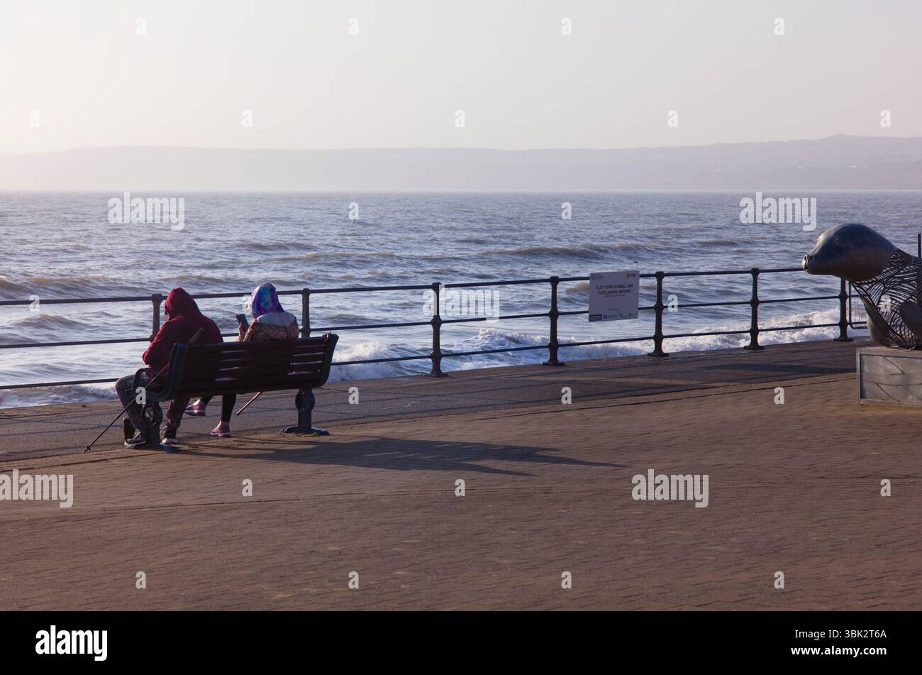 Zwei Walker sitzen auf dem Filey-Abschlussball und schauen sich ihre Handys an Stockfoto