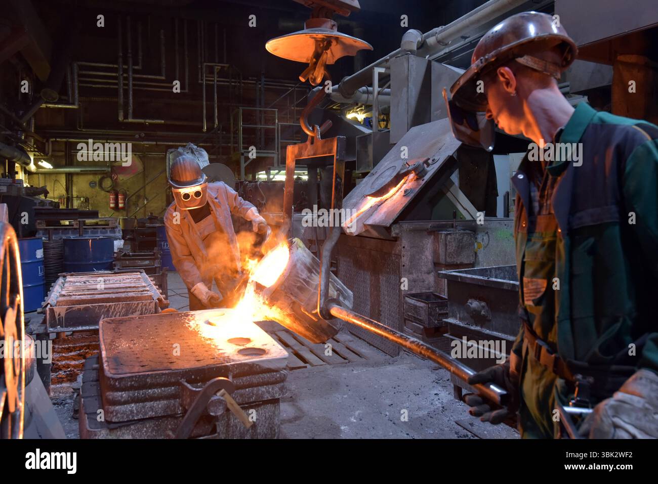 Arbeitnehmer in einer Gießerei gießen ein Werkstück aus Metall - Sicherheit bei der Arbeit und Teamarbeit Stockfoto
