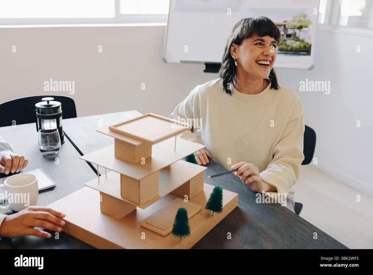 Eine Projektmanagerin lächelt, während sie in einem Büro über ein architektonisches Baumodell spricht. Professionelle Zusammenarbeit und kreative Designideen sind vorhanden Stockfoto
