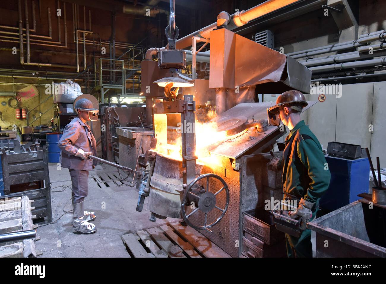 Arbeitnehmer in einer Gießerei gießen ein Werkstück aus Metall - Sicherheit bei der Arbeit und Teamarbeit Stockfoto