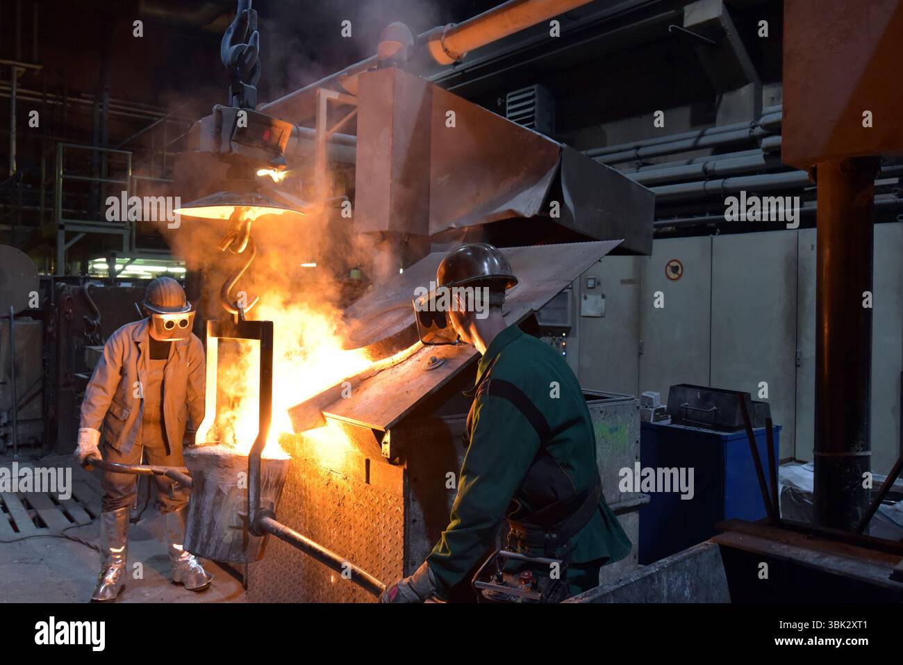 Arbeitnehmer in einer Gießerei gießen ein Werkstück aus Metall - Sicherheit bei der Arbeit und Teamarbeit Stockfoto