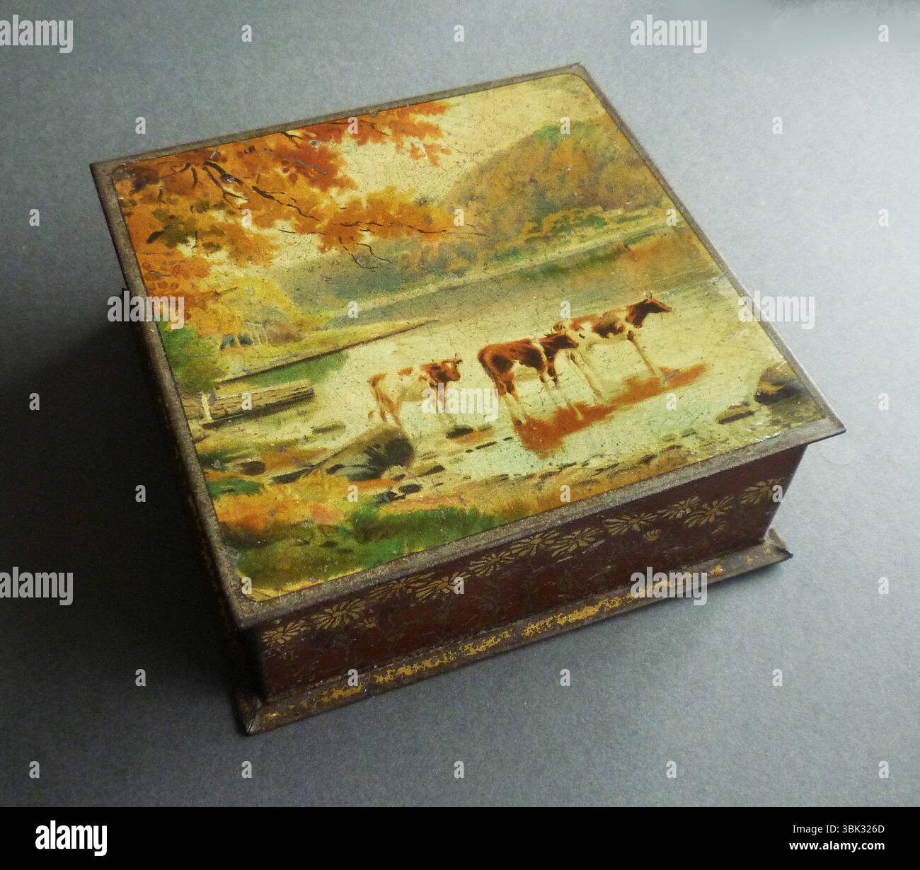 Eine antike Keksdose, die um 1910 in England von der Co-operative Wholesale Society Ltd, Crumpsall, hergestellt wurde. Der Deckel ist mit einer attraktiven Hirtenszene dekoriert, die Kühe zeigt, die aus einem See mit Hügeln in der Ferne trinken. Die Seiten sind mit Gänseblümchen im Jugendstilstil dekoriert. Die Crumpsall Biscuit Works der Co-operative Wholesale Society wurden um 1873 in Lower Crumpsall, Manchester, eröffnet. Die Fabrik hatte vier Abteilungen: Die Keksfabrik, die Kuchenfabrik, die Süßigkeiten- und Toffee-Abteilung und die Drogen- und Verbrauchsartikel-Abteilung. Stockfoto