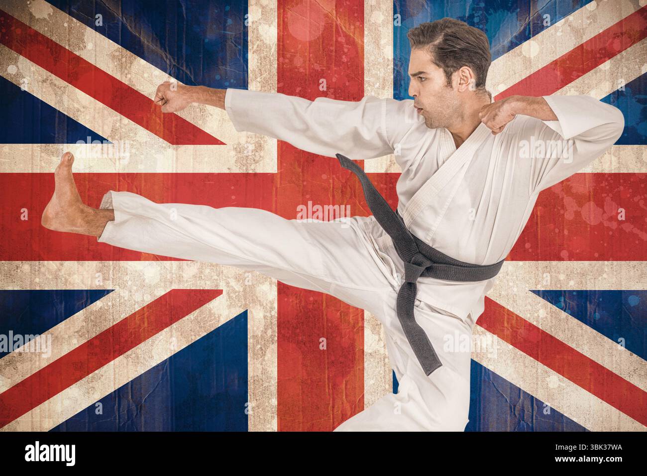Der Schwarzgürtel-Kampfkünstler führt einen High Side Kick in flacher hölzerner Union Jack-Kulisse aus Stockfoto