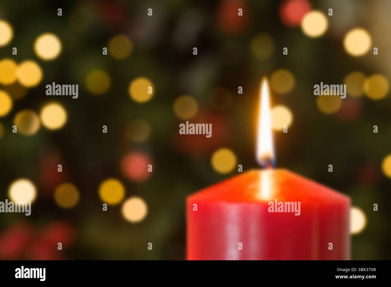 Flache Kerze mit roter Säule, die vor Flammen leuchtet und Licht über warmes Bokeh und grünes Laub wirft Stockfoto