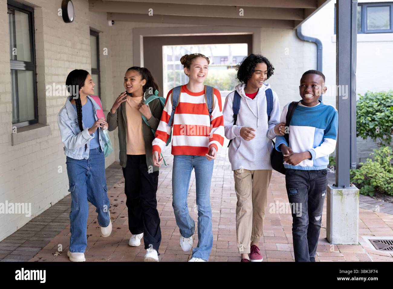 Verschiedene Gruppen von Schülern laufen zusammen in der Schule, lächeln und plaudern glücklich Stockfoto