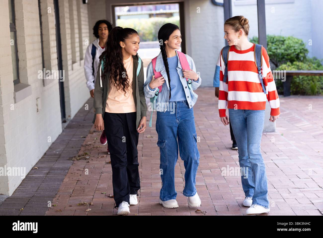 Gruppe von verschiedenen Schülern, die zusammen außerhalb der Schule laufen, lächeln und plaudern glücklich Stockfoto
