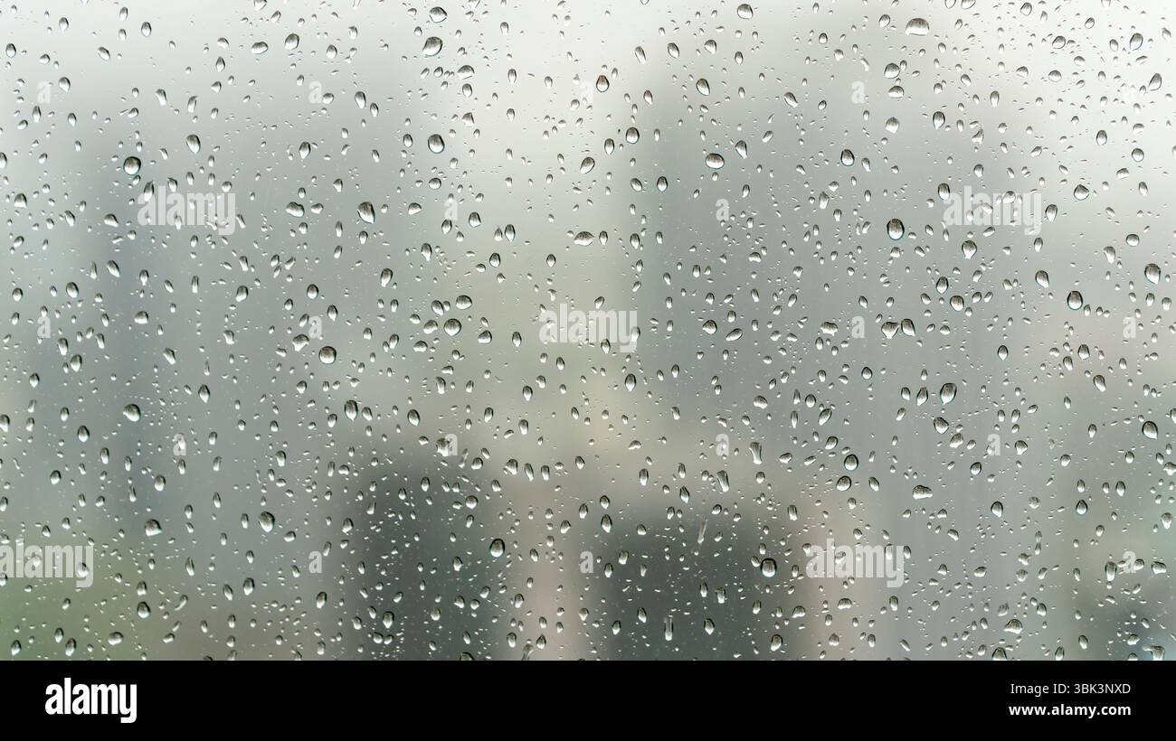 Blick auf den regnerischen Tag durch ein Fenster mit Wassertröpfchen, die sich an das Glas schmiegen, verschwimmen das urbane Stadtbild draußen und schaffen eine ruhige und introspektive Atmosphäre Stockfoto