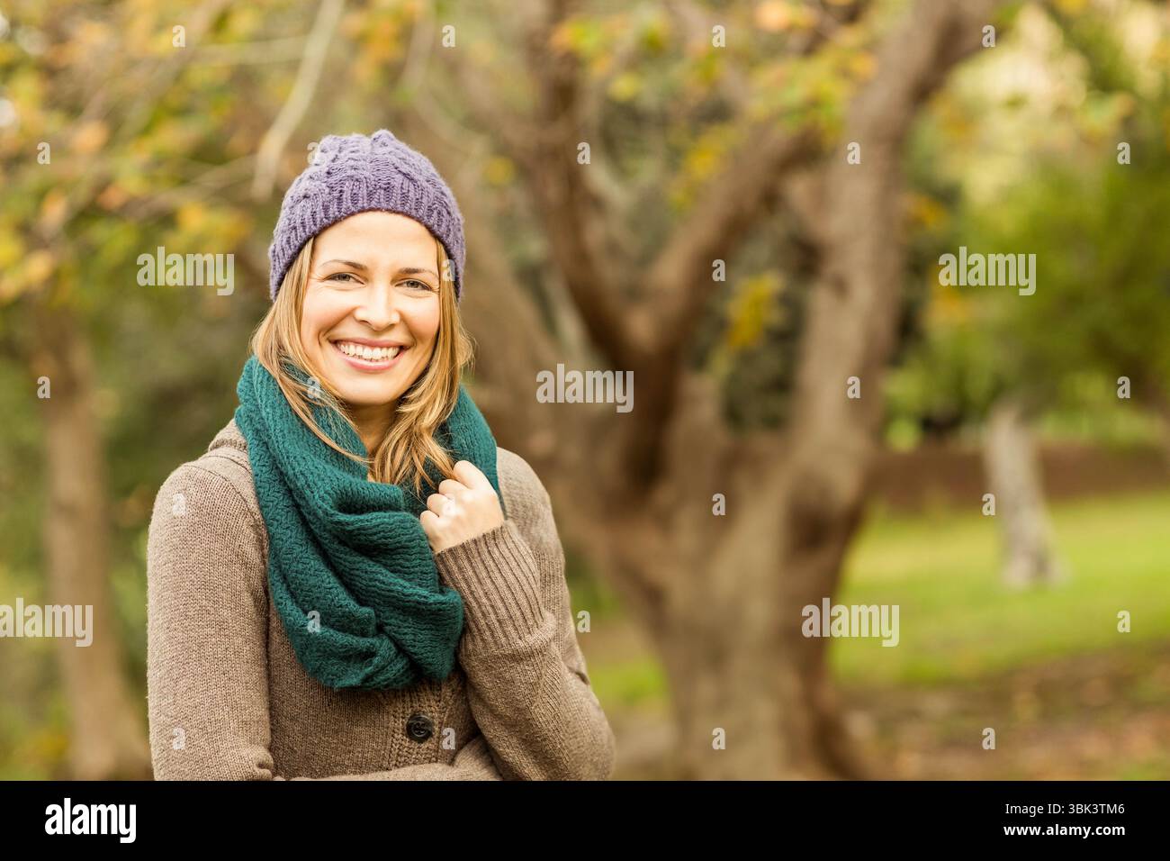 Frau, die im Herbst im Park steht und lila Mütze, grüner Schal und braune Strickjacke trägt, Kopierraum Stockfoto