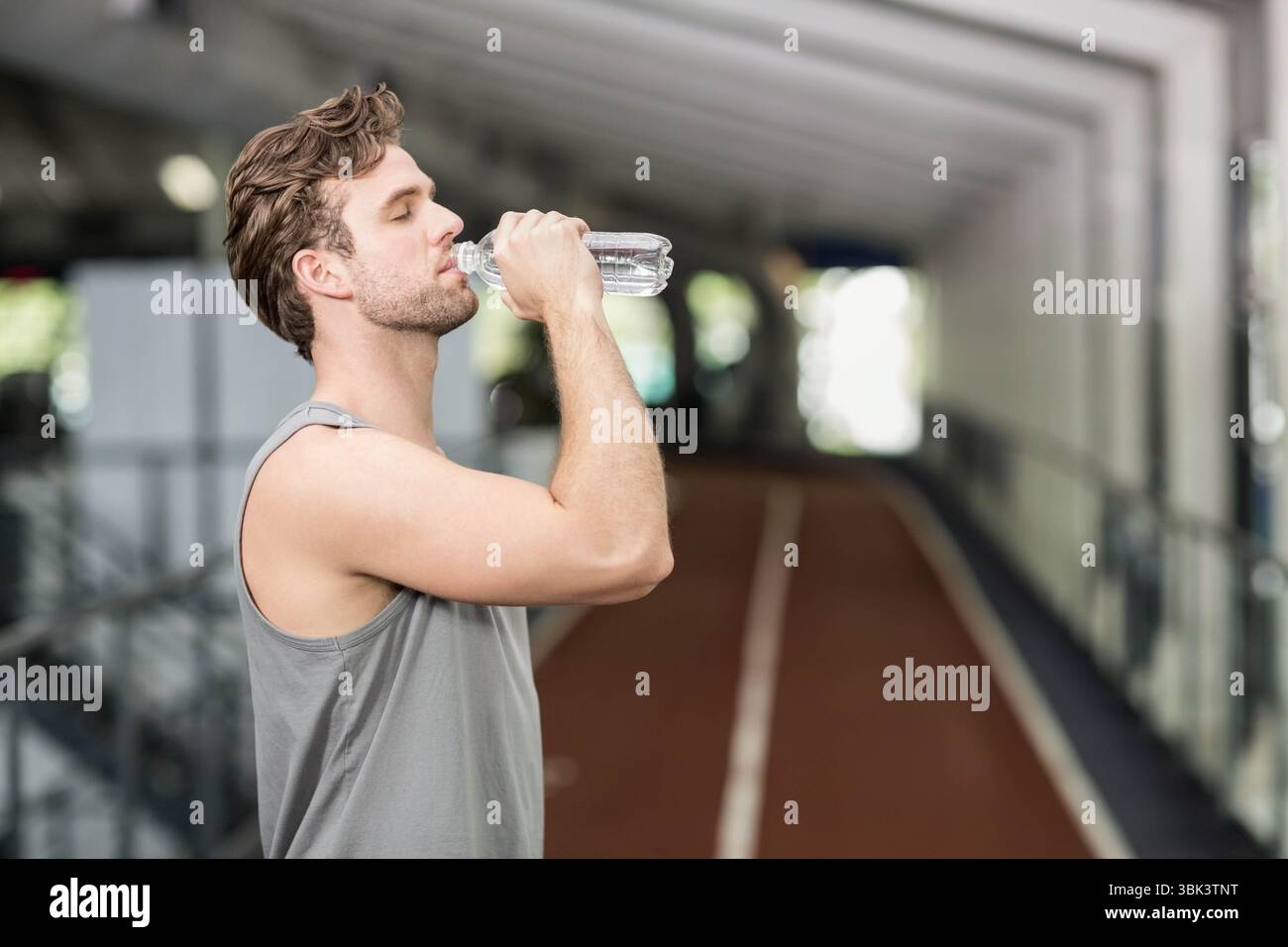 Muskulöser Mann trinkt Wasser aus Plastikflasche auf der roten Schiene in den Gängen des Fitnessraums, Kopierraum Stockfoto