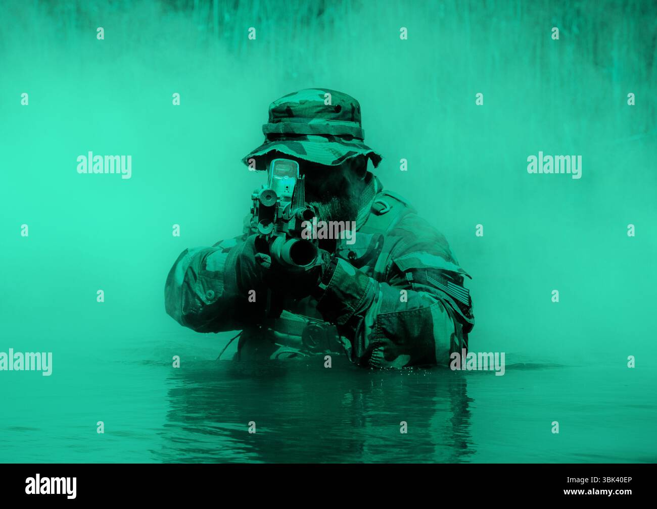 Soldat in Tarnuniform und Hut, der ein Gewehr anvisiert, während er halb in Wasser getaucht ist, mit grünem Nebel. Stockfoto