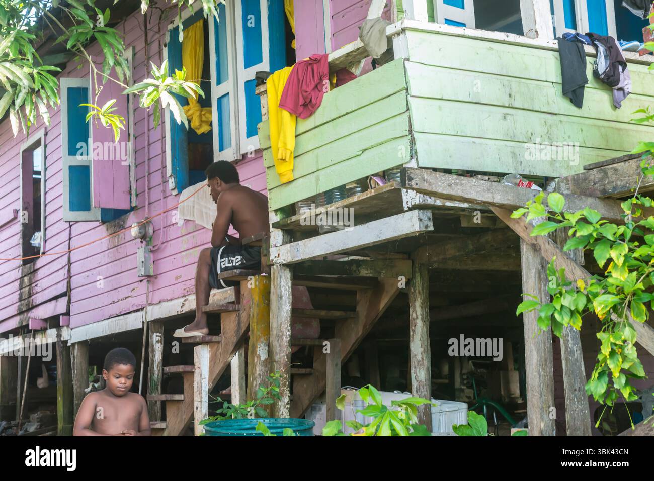 Vater und Sohn sitzen auf der Treppe ihres alten hölzernen, bunten Pfahlhauses in Old Bank, Isla Bastimentos, Bocas del Toro, Panama Stockfoto