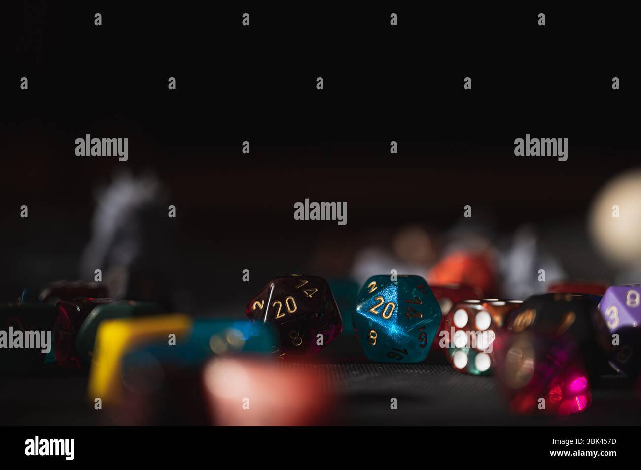 Eine Sammlung von bunten RPG-Würfeln auf einer schwarzen Oberfläche, mit einem blauen D20, das „20" zeigt. Die Komposition hinterlässt oben einen großen, dunklen Kopierraum Stockfoto