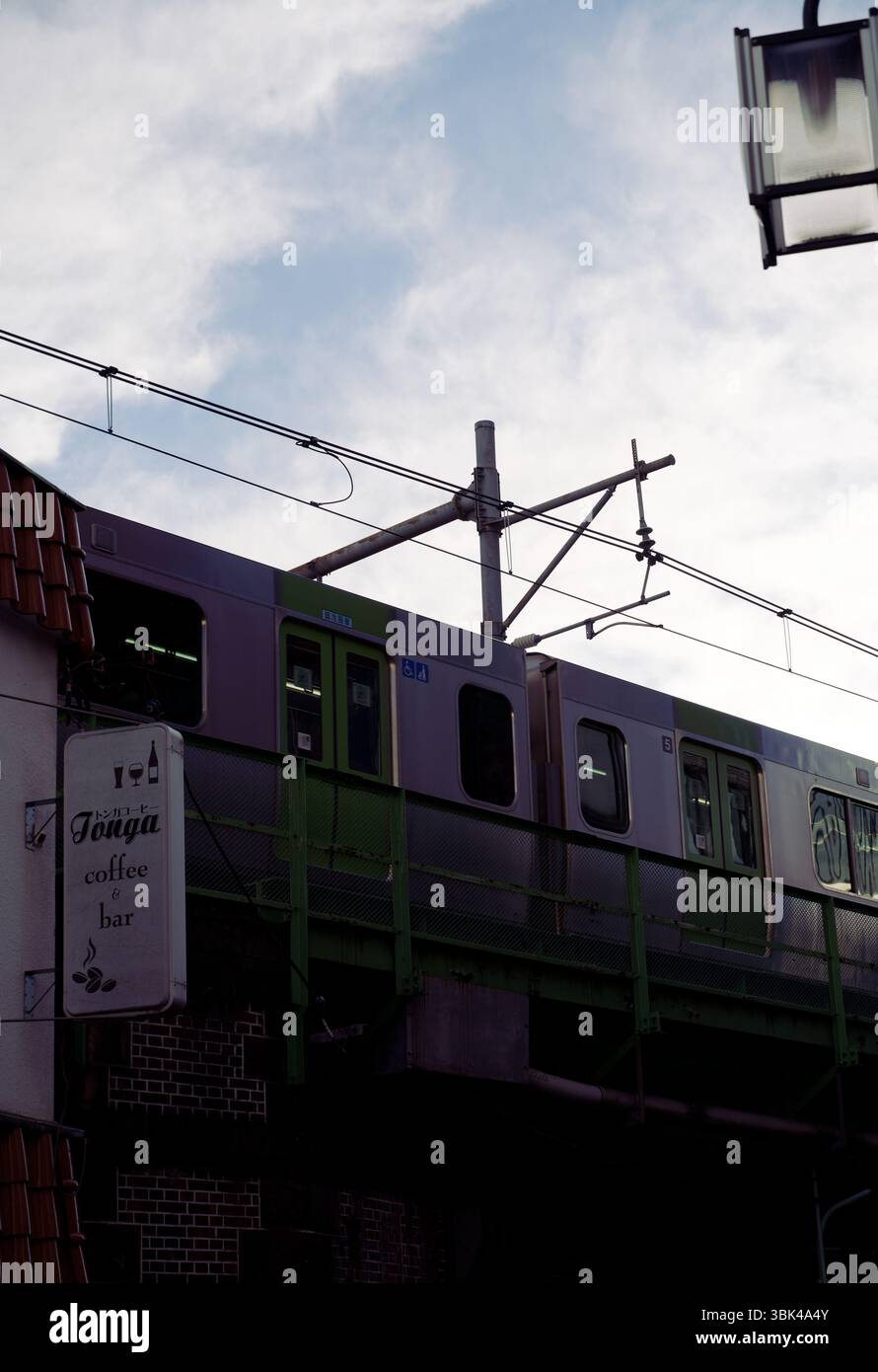 Die U-Bahn eines JR Yamanote Line-Zuges gleitet in der Abenddämmerung an einer ruhigen Café-Bar vorbei Stockfoto