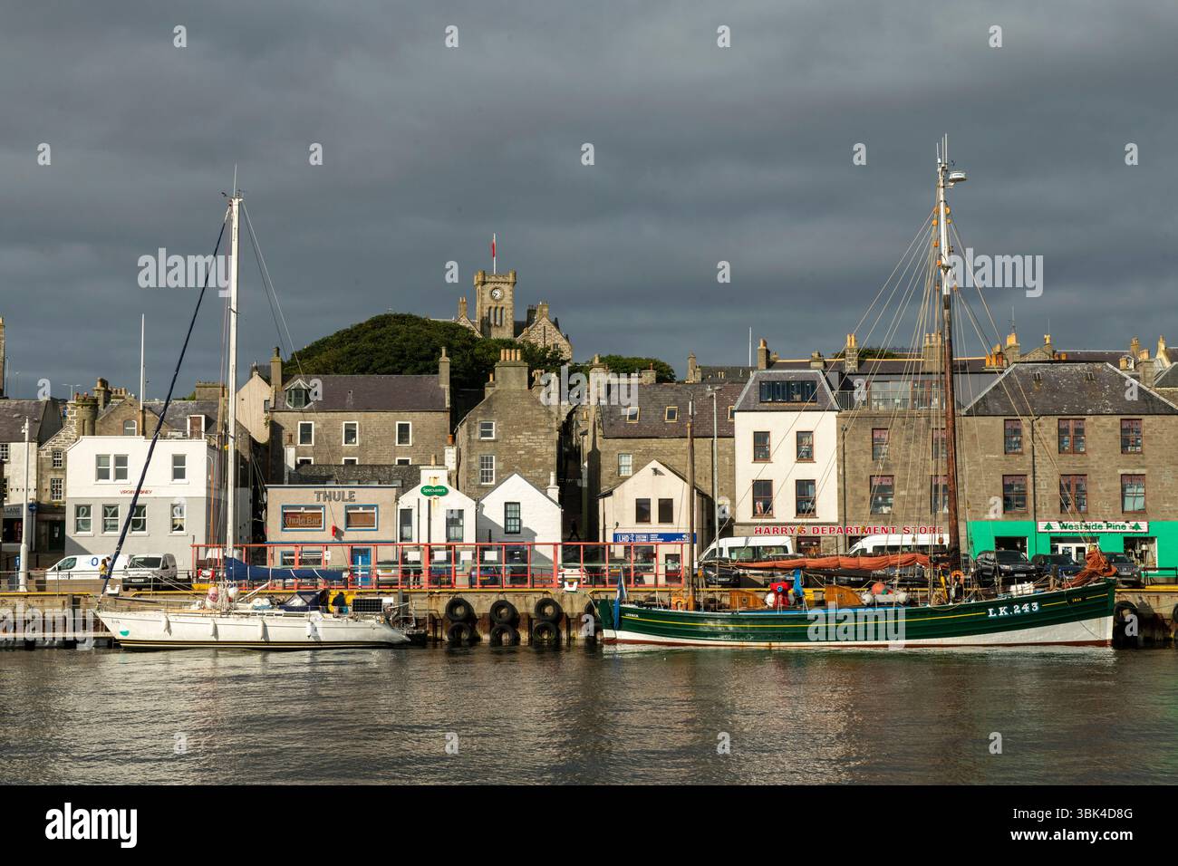 Lerwick Harbour sonnt sich in der frühen Sonne, während sich über dem Himmel dunkler, brütender Himmel erhebt – ein dramatischer Kontrast zu Shetlands wechselndem Wetter. Stockfoto