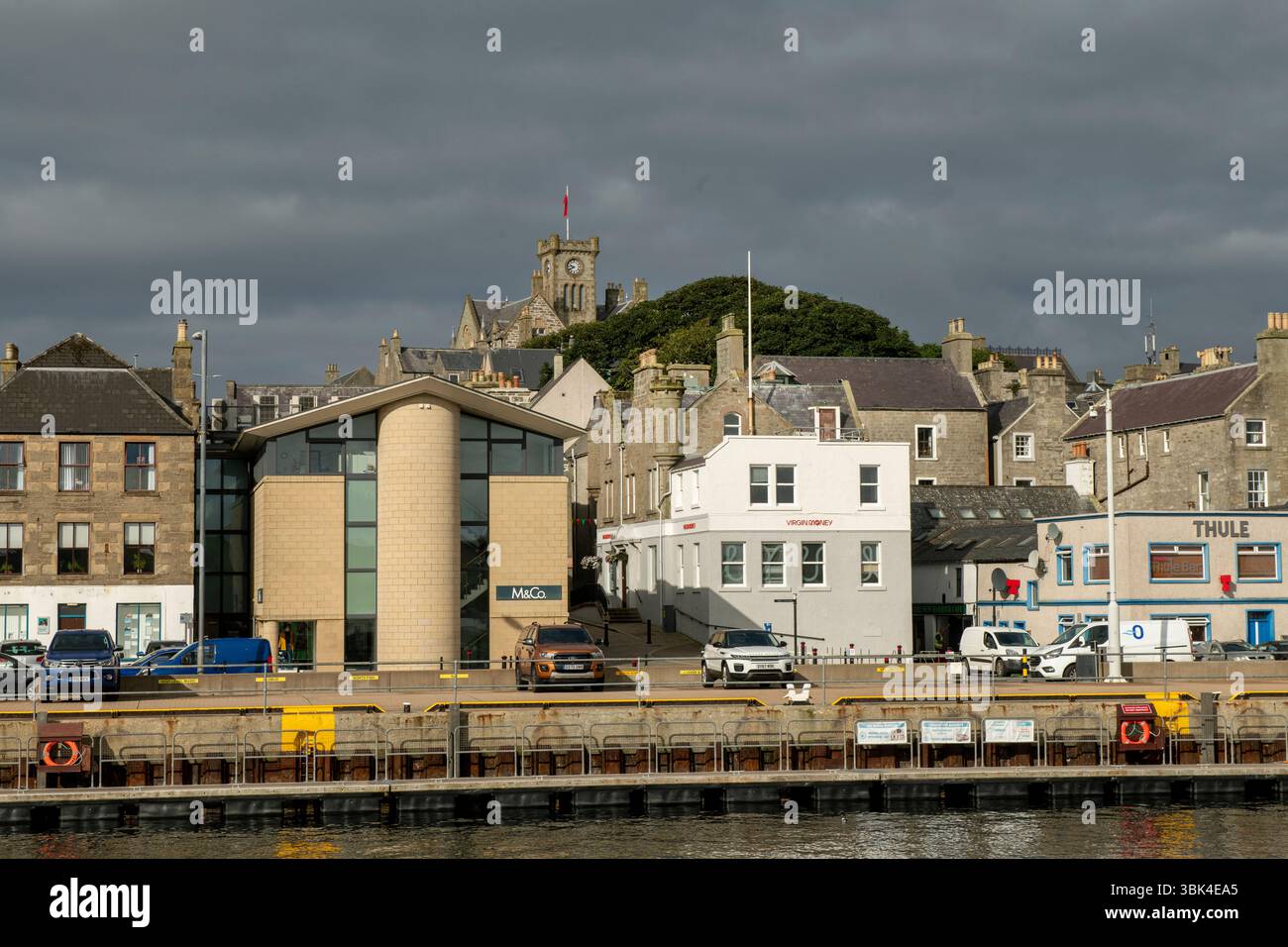 Lerwick Harbour sonnt sich in der frühen Sonne, während sich über dem Himmel dunkler, brütender Himmel erhebt – ein dramatischer Kontrast zu Shetlands wechselndem Wetter. Stockfoto