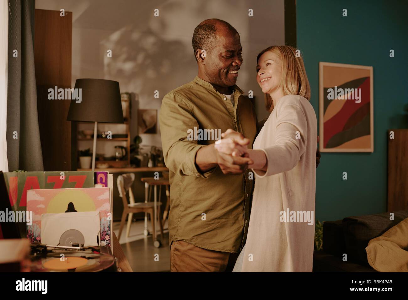 Seniorenpaar, das zusammen tanzt und im gemütlichen Wohnzimmer lächelt Stockfoto