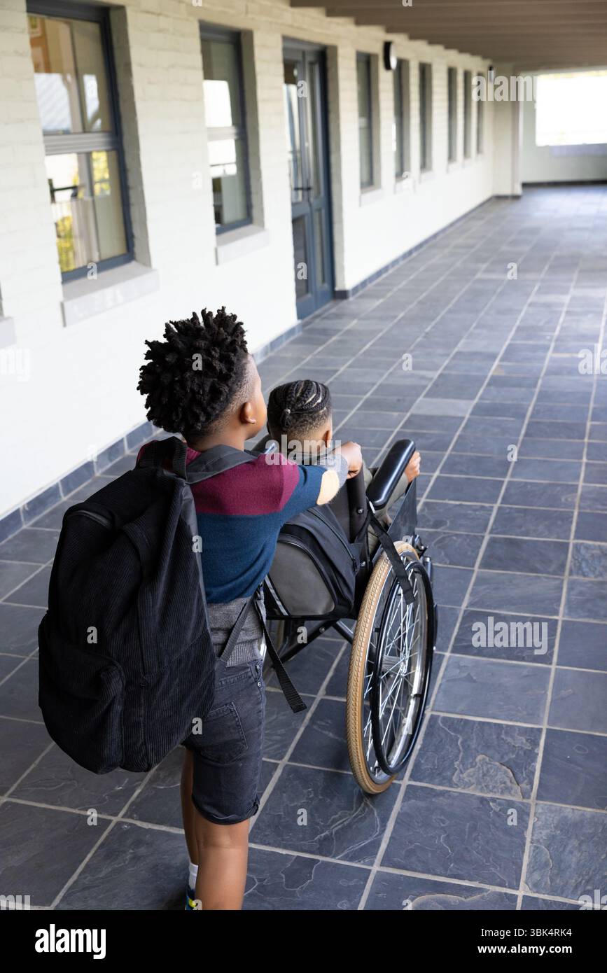 Wir laufen zusammen im Schulflur, verschiedene Jungs zeigen Freundschaft, einer schiebt den Rollstuhl Stockfoto