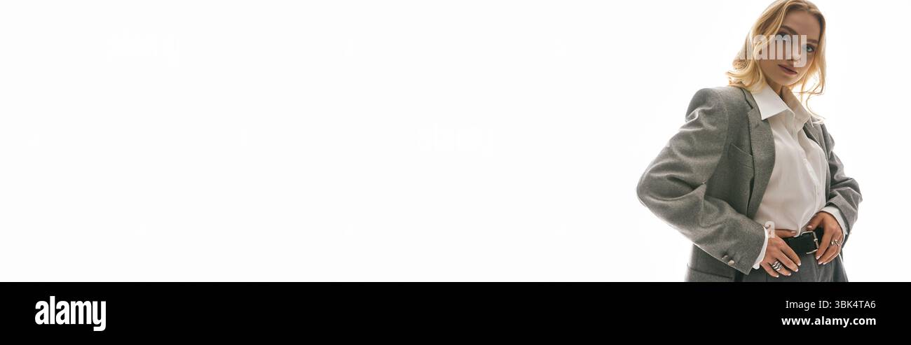 Trendige junge Frau posiert selbstbewusst in modischer Kleidung vor einem hellen Hintergrund. Stockfoto