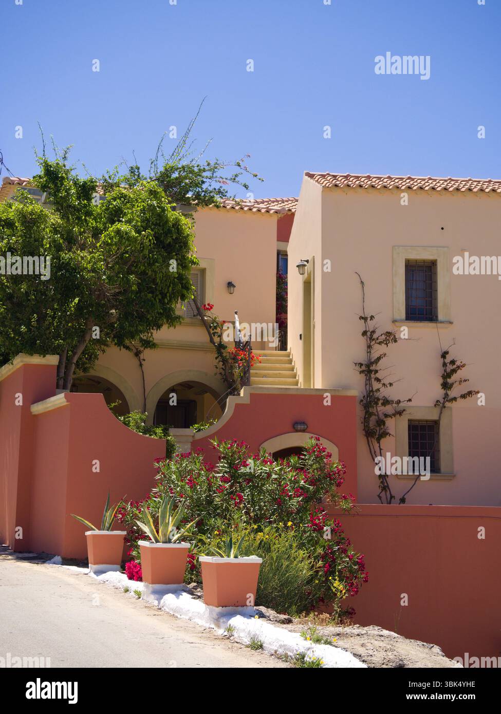 Sonnendurchflutetes mediterranes Haus mit roten Wänden, gelber Fassade, Topfpflanzen und blühenden Bougainvillea. Stockfoto