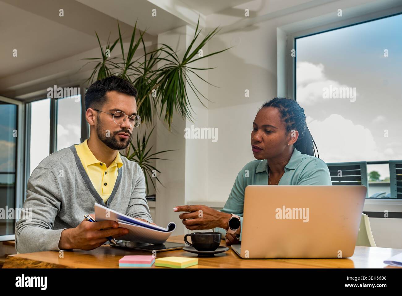 Zwei Geschäftsleute arbeiten in einem Büro zusammen, um Dokumente zu prüfen und Ideen mit einem Laptop während eines gemeinsamen Meetings zu analysieren Stockfoto