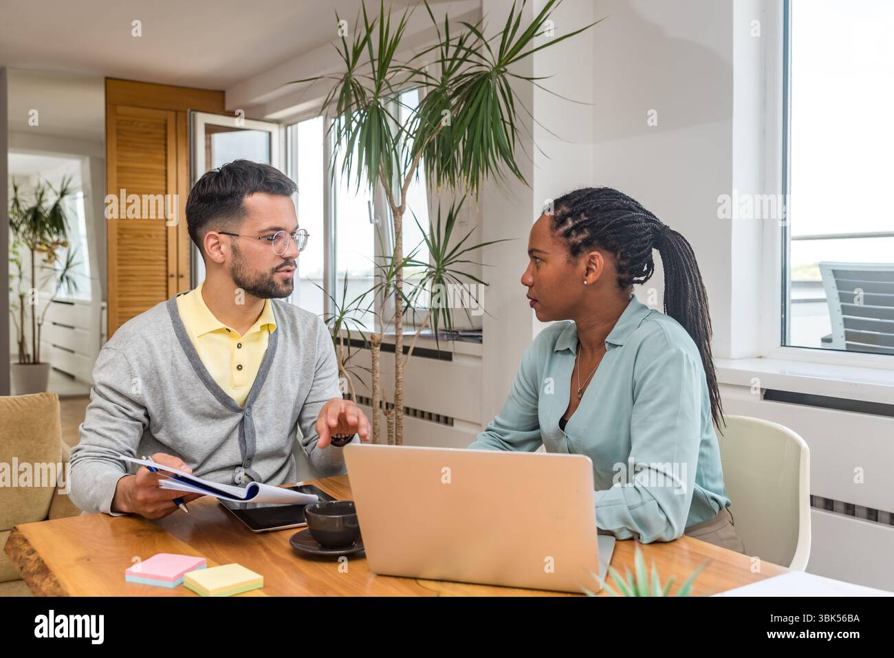 Zwei Geschäftsleute arbeiten in einem Büro zusammen, um Dokumente zu prüfen und Ideen mit einem Laptop während eines gemeinsamen Meetings zu analysieren Stockfoto