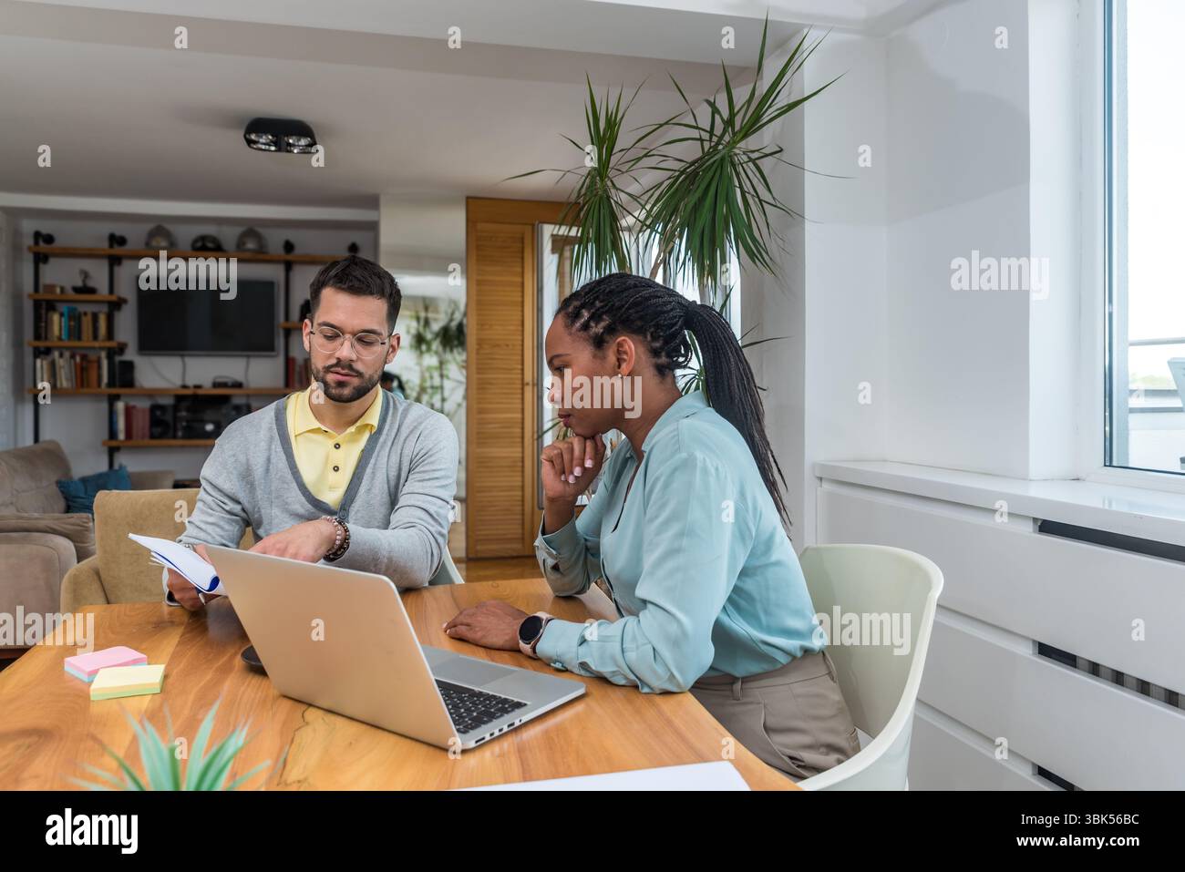 Zwei Geschäftsleute arbeiten in einem Büro zusammen, um Dokumente zu prüfen und Ideen mit einem Laptop während eines gemeinsamen Meetings zu analysieren Stockfoto