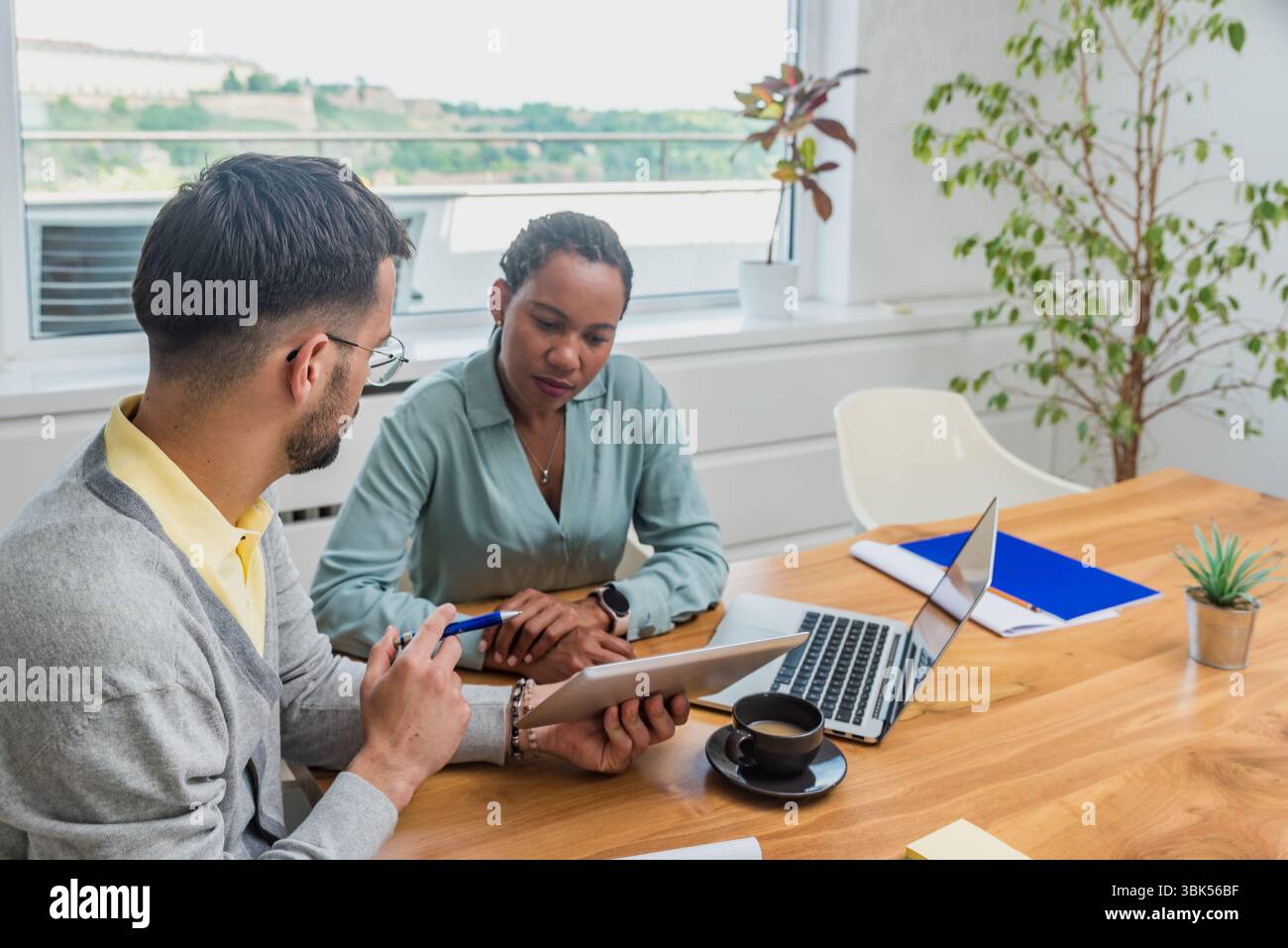 Zwei Geschäftsleute arbeiten in einem Büro zusammen, um Dokumente zu prüfen und Ideen mit einem Laptop während eines gemeinsamen Meetings zu analysieren Stockfoto