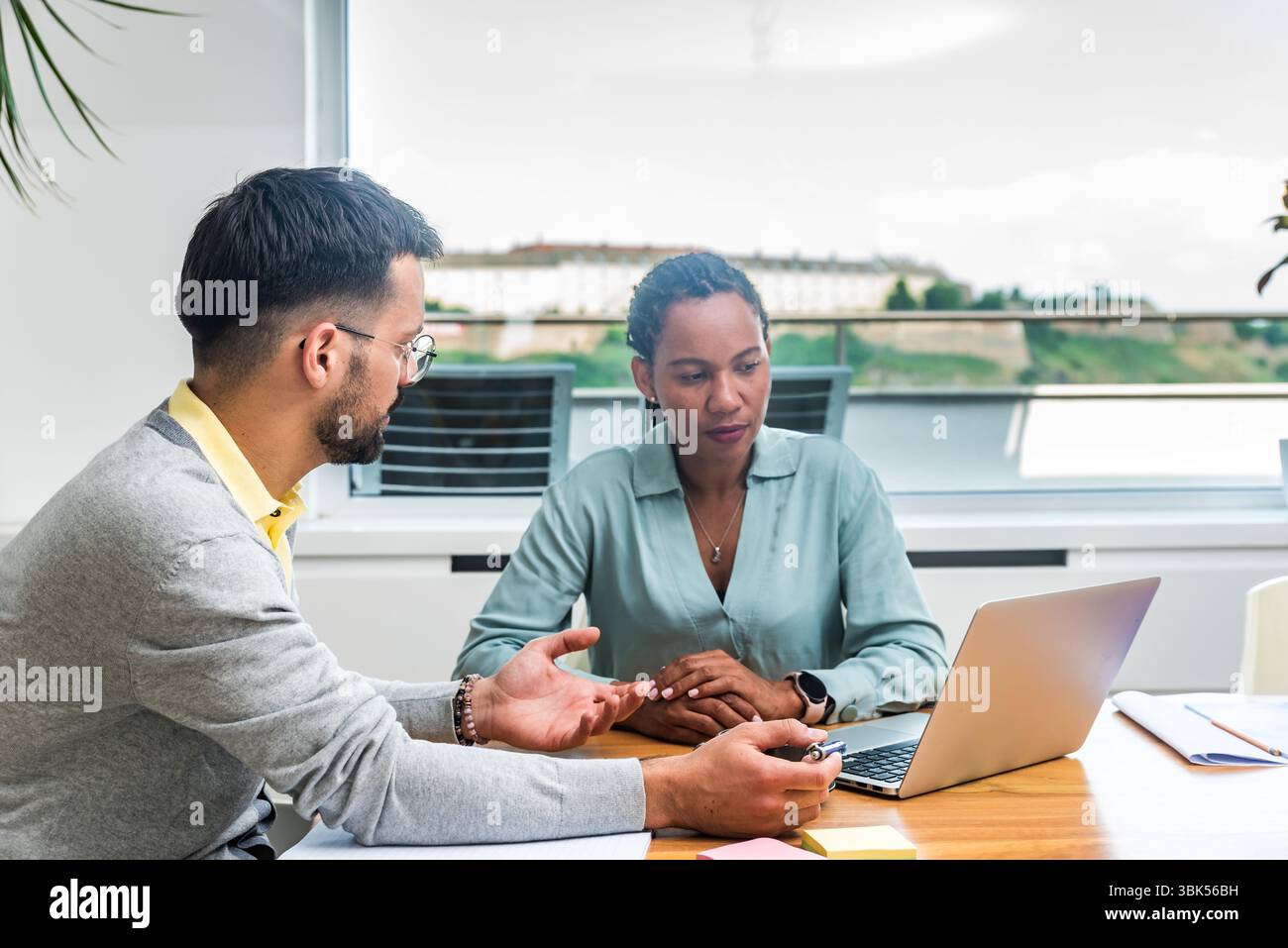 Zwei Geschäftsleute arbeiten in einem Büro zusammen, um Dokumente zu prüfen und Ideen mit einem Laptop während eines gemeinsamen Meetings zu analysieren Stockfoto