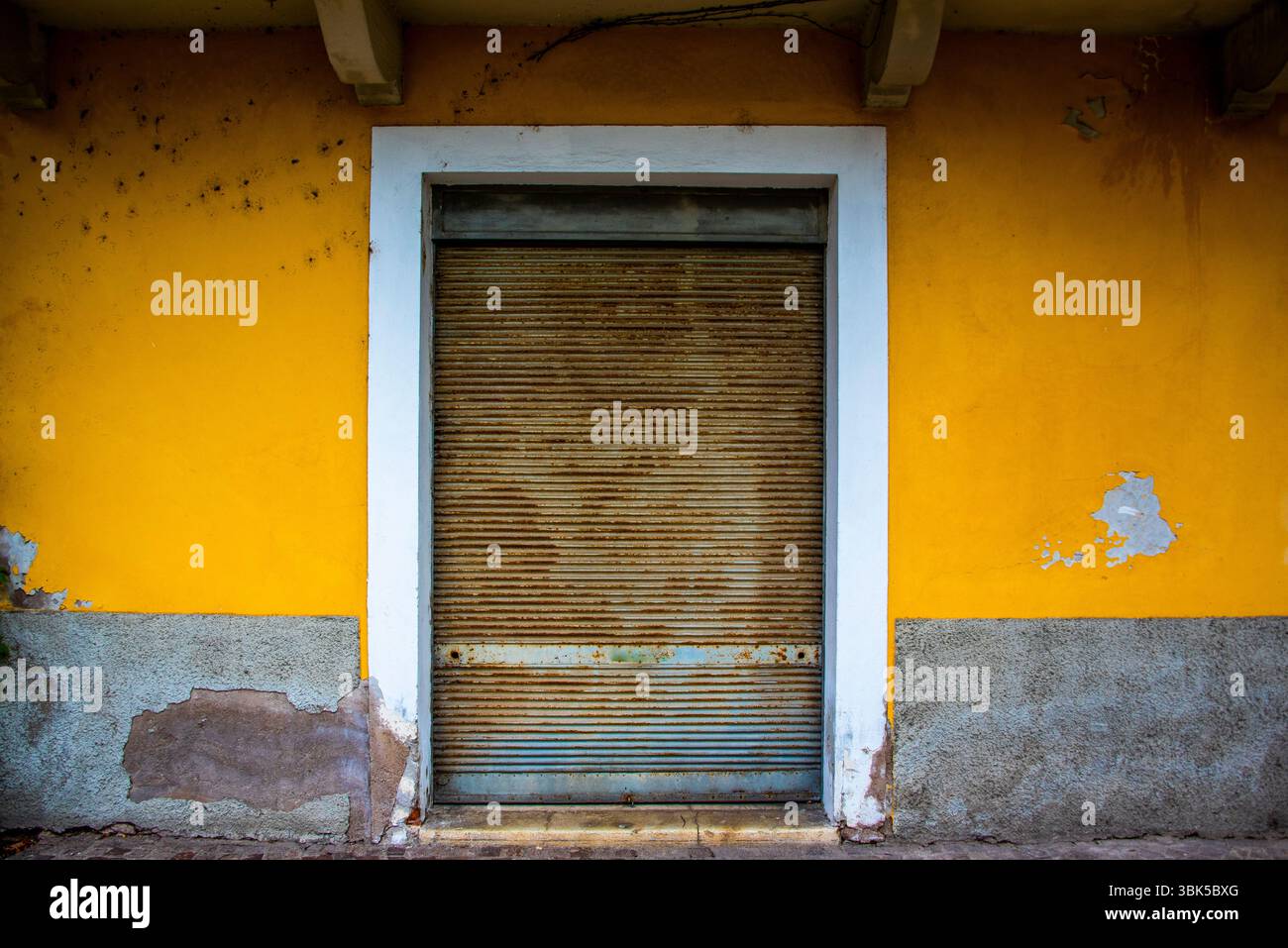 Antike rostige geschlossene Blende in einer ockergelben Wand in Riva del Garda, Trient, Italien Stockfoto