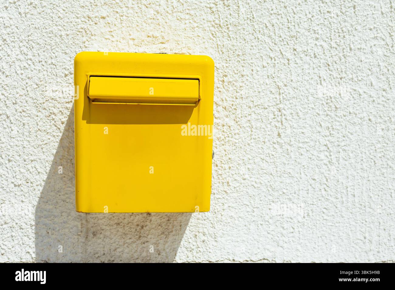 Gelbe Mailbox an hellweißer Wand. Postdienst, Kommunikationssymbol und Straßendetails in sonniger Umgebung. Kopierbereich Stockfoto