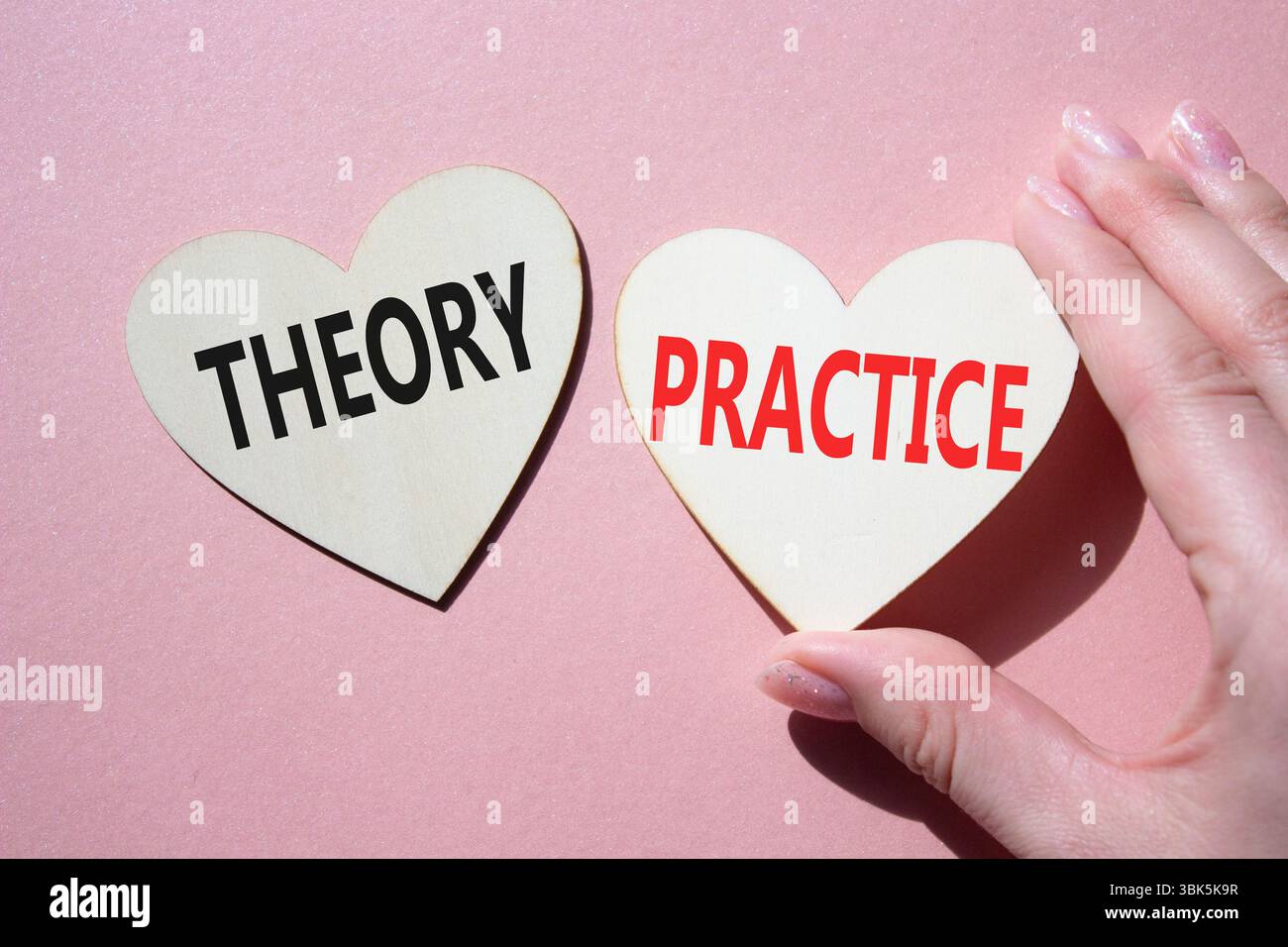 Theorie- oder Praxissymbol. Konzeptwort Theorie oder Praxis auf hölzernen Herzen. Geschäftsmann Hand. Schöner rosafarbener Hintergrund. Business und Theorie oder Praxis Stockfoto