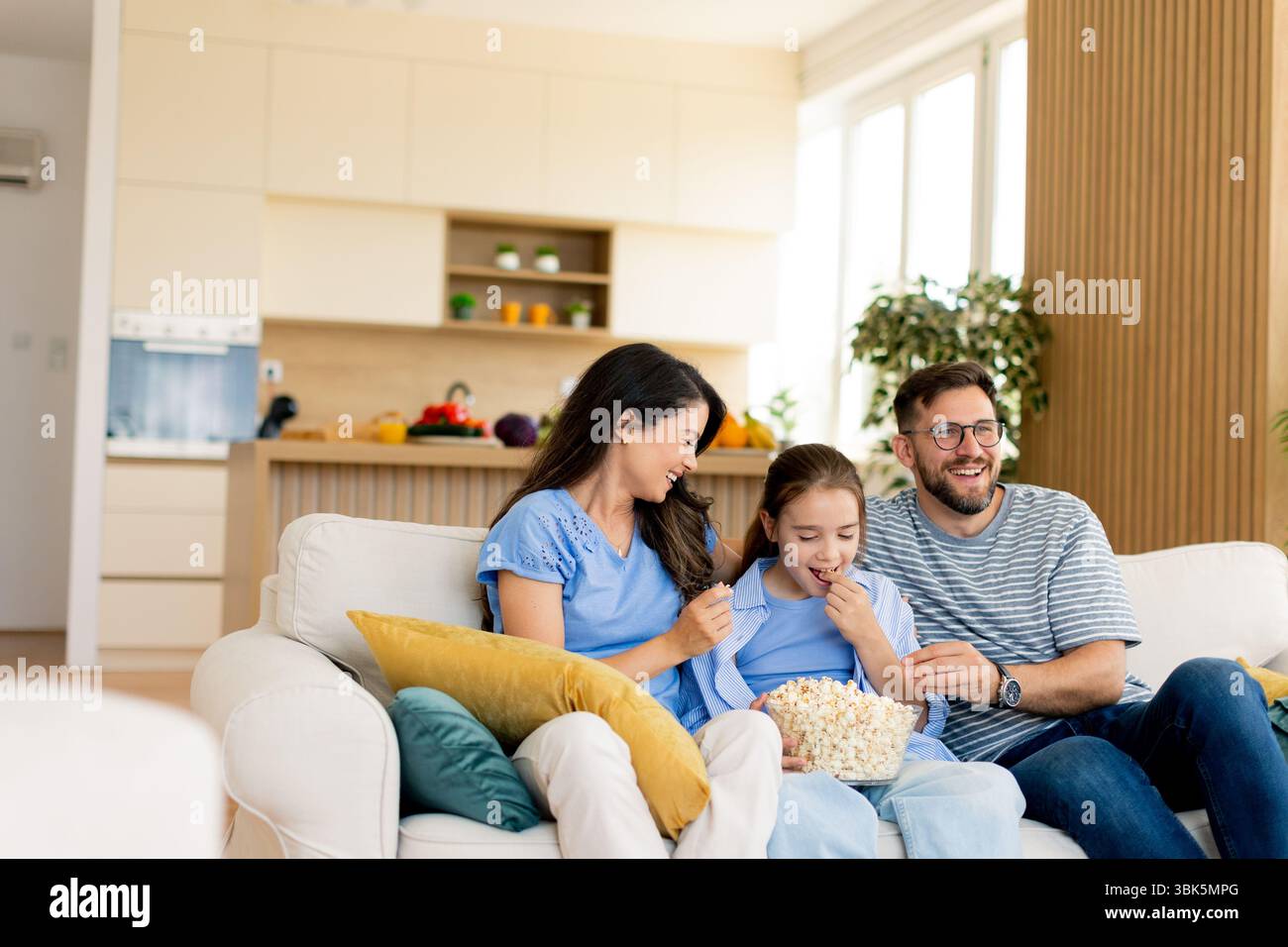 In einem warmen und einladenden Wohnzimmer teilt sich eine Familie eine Schüssel Popcorn, während sie zusammen in einem Film eine gute Zeit genießt. Stockfoto
