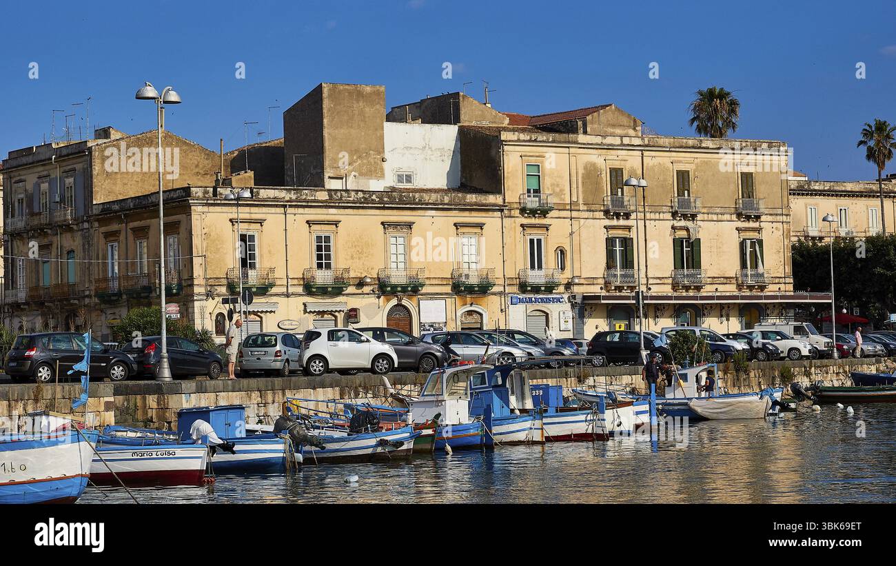 Fischerboote in einem Hafen vor historischen Gebäuden und geparkten Autos, Bootsfahrt um die Insel Ortigia, Isola di Ortigia, Syrakus, Sizilien Stockfoto